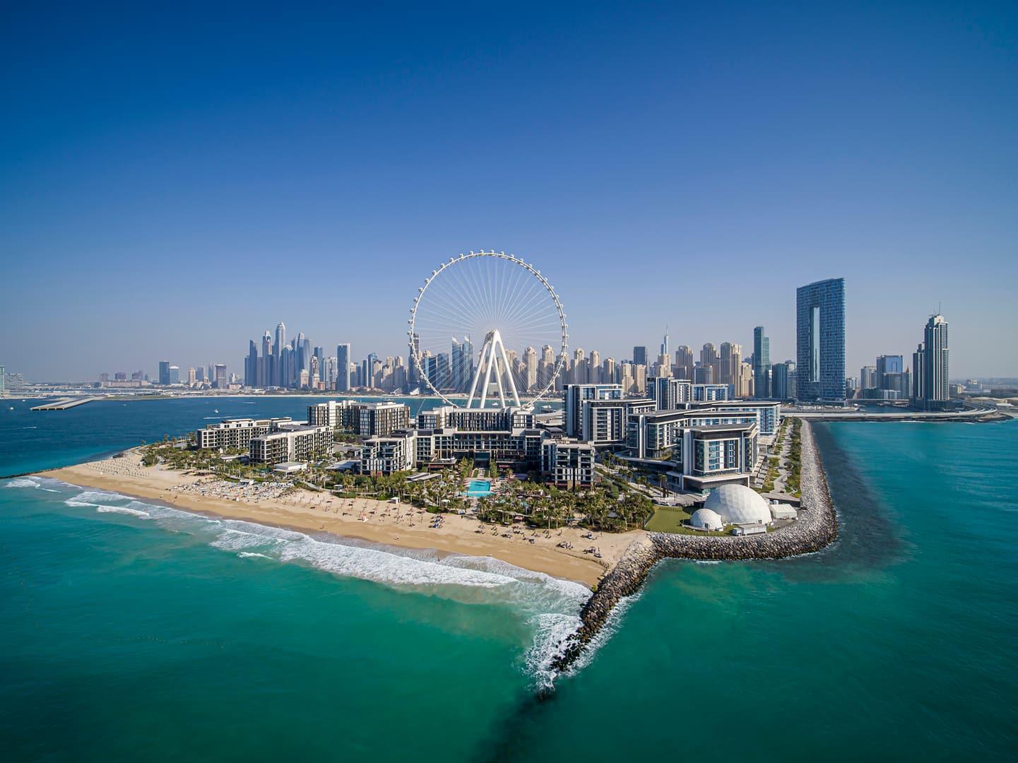 Aerial view of Bluewaters Island featuring Banyan Tree Dubai with Ain Dubai Ferris wheel at the center, surrounded by turquoise waters and the iconic Dubai Marina skyline in the background.