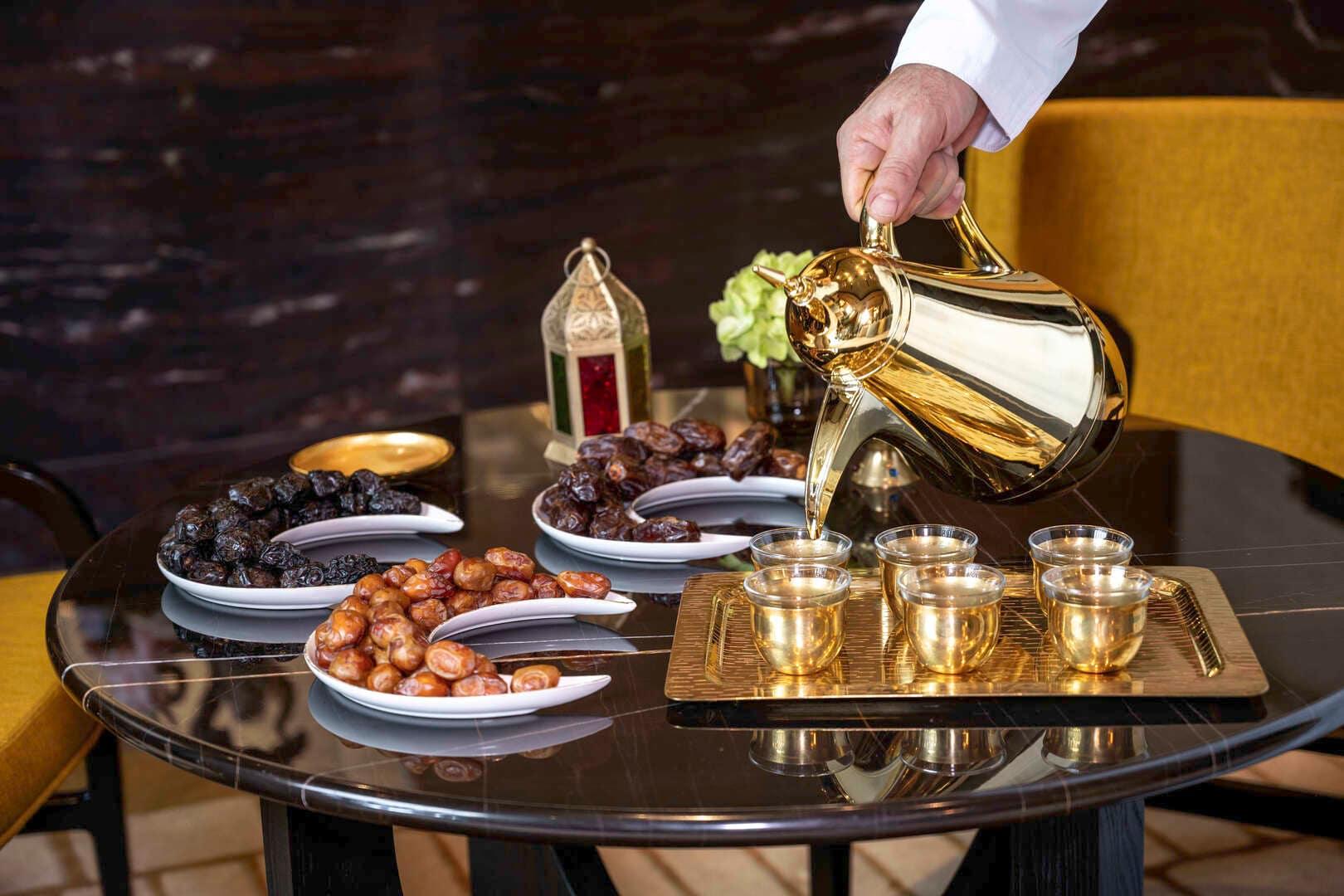 Traditional Arabic coffee being poured from a golden dallah into cups, served alongside an elegant assortment of dates on a black marble table at Banyan Tree Dubai.