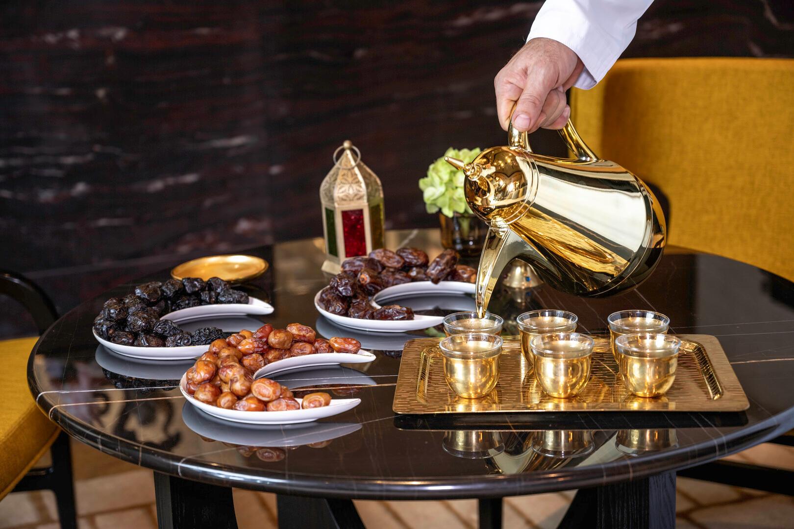 Traditional Arabic coffee being poured from a golden dallah into cups, served alongside an elegant assortment of dates on a black marble table at Banyan Tree Dubai.