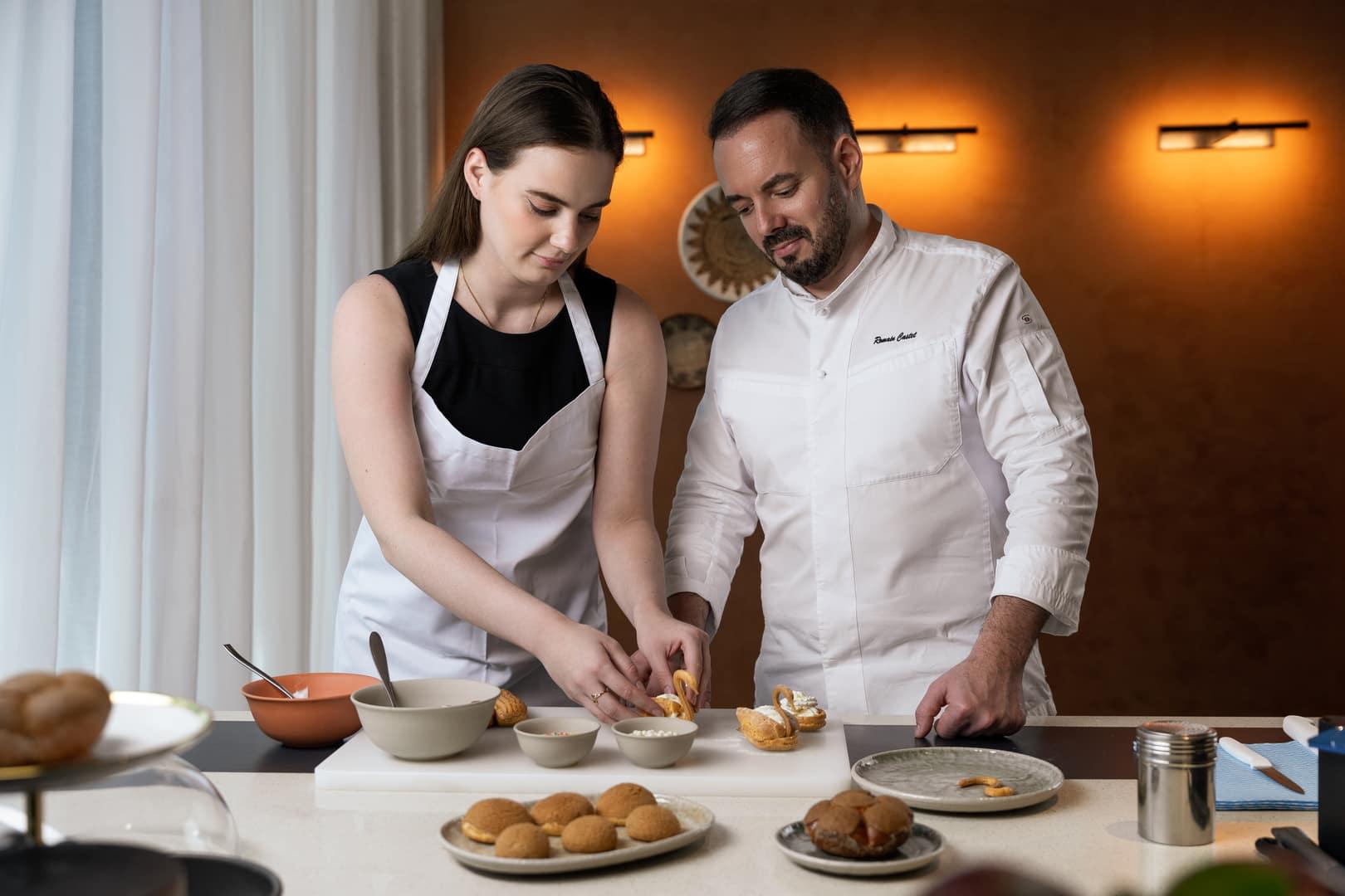 Chef guides a young woman through a hands-on pastry-making session in the French Patisserie Lab at Banyan Tree Dubai, surrounded by bowls of ingredients and finished desserts.