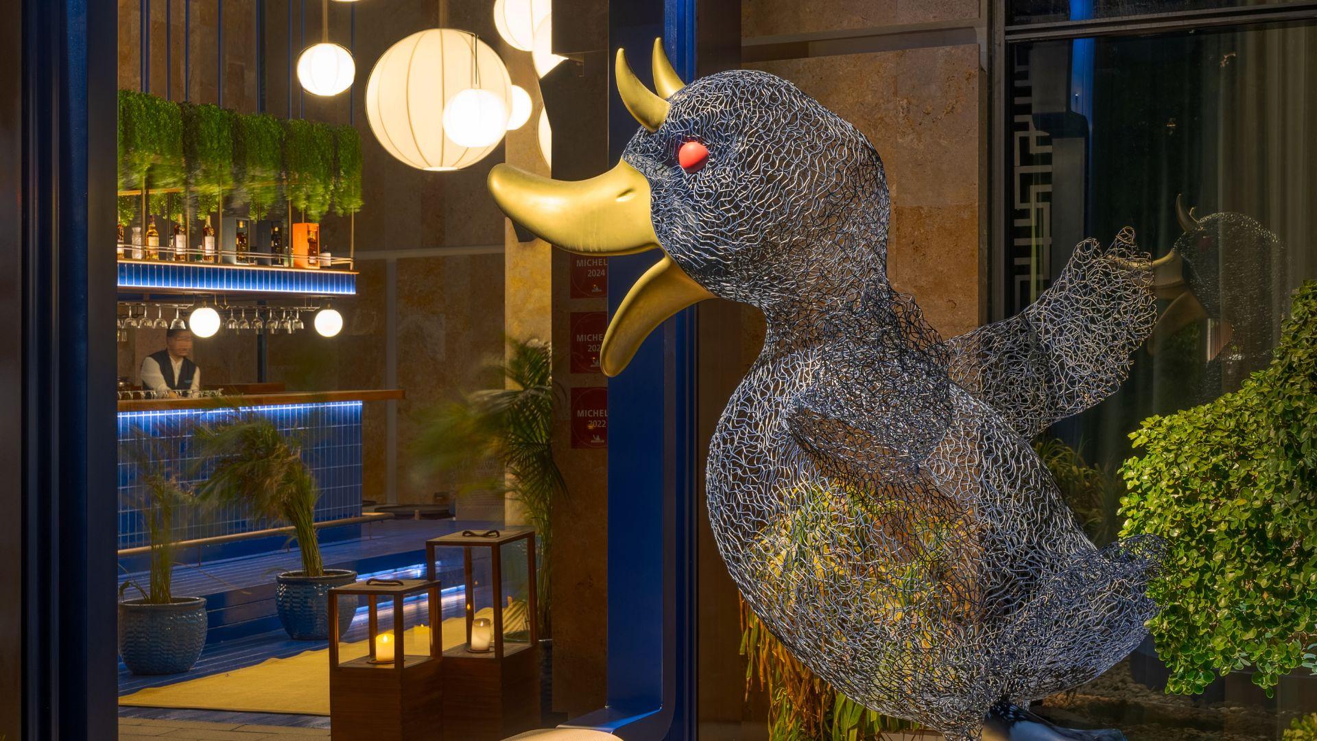 Wire sculpture of a duck at the entrance of Demon Duck, Banyan Tree Dubai, with a stylish bar in the background