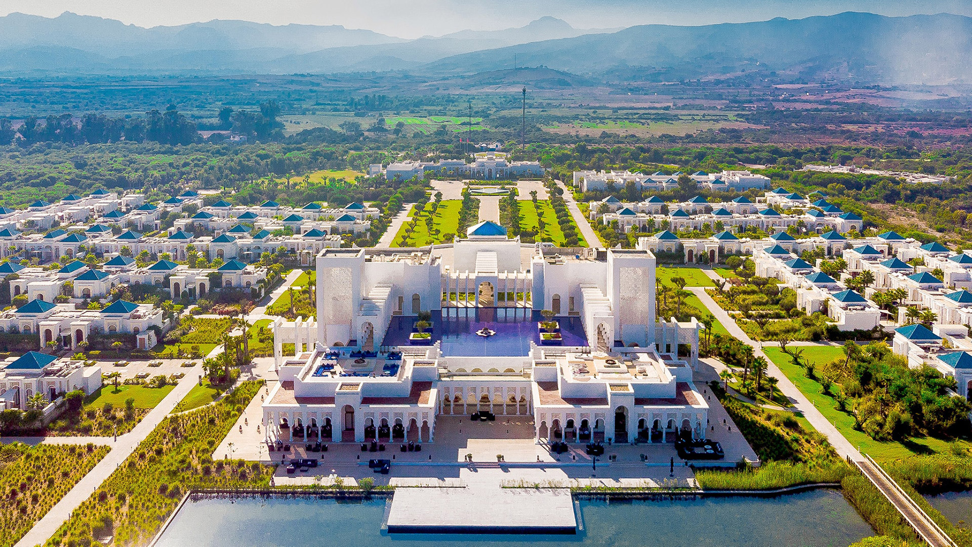 Aerial view showcasing Banyan Tree Tamouda Bay Morocco white villas and lush gardens amid mountainous backdrop.