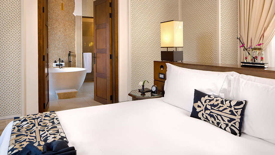 Bed with patterned cushions faces an open bathroom with a tub at Banyan Tree Tamouda Bay Serenity Pool Villa.