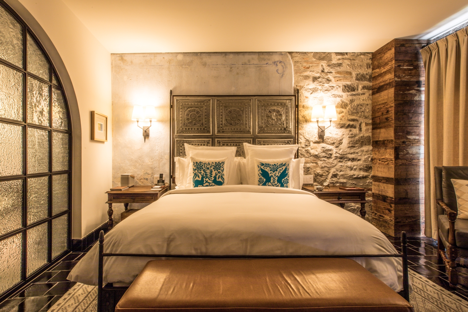 Luxurious bed with decorative pillows in Banyan Tree Puebla Urban junior suite king, set against rustic stone walls.