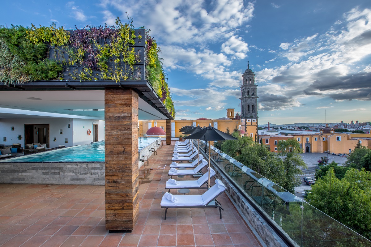 Rooftop pool overlooks city; loungers line the terrace at Banyan Tree Puebla, luxury resorts in Puebla, Mexico.