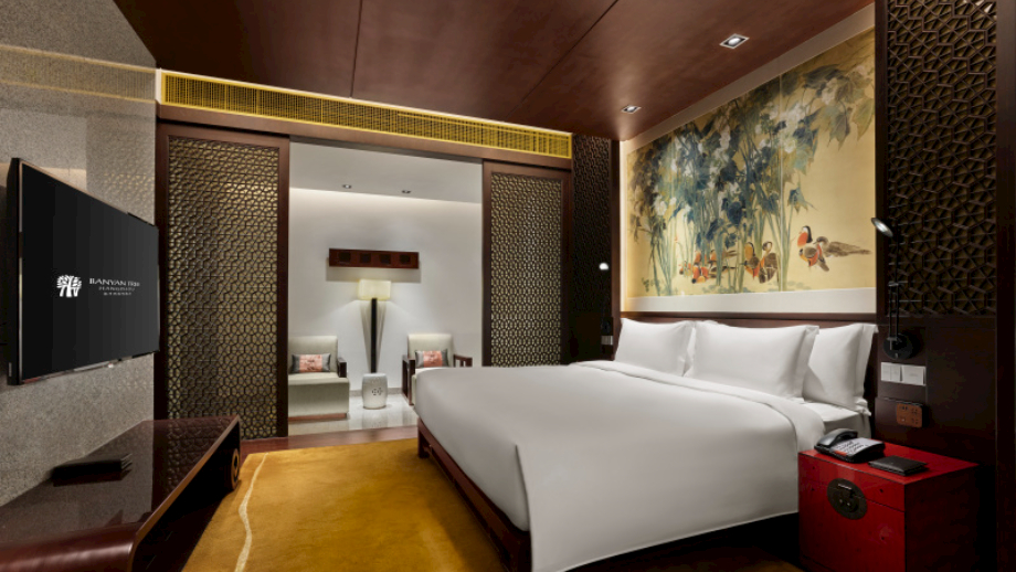 Luxury bed with ornate paneling, TV on, serene décor in Banyan Tree Hangzhou room.