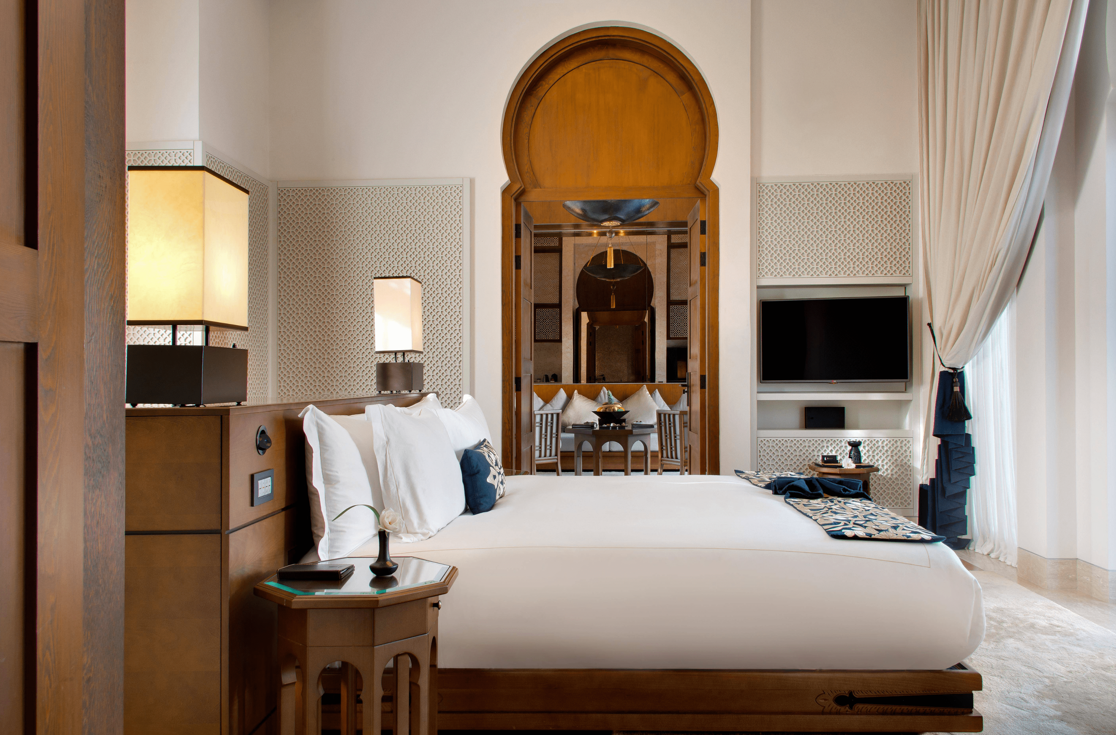 Luxurious bed with plush pillows in Banyan Tree Tamouda Bay Wellbeing sanctuary pool villa, ornate archway leading to dining area.