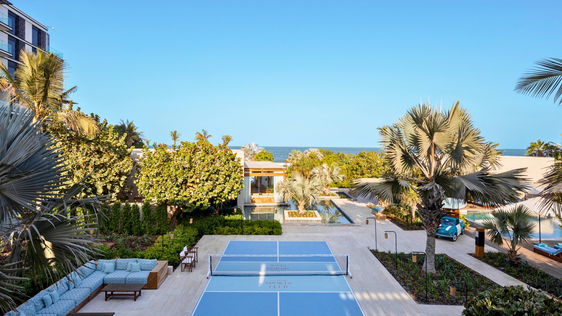 Tennis court overlooked by lush gardens, ocean in view; Banyan Tree Dubai's La-Cantine beach serene setting.