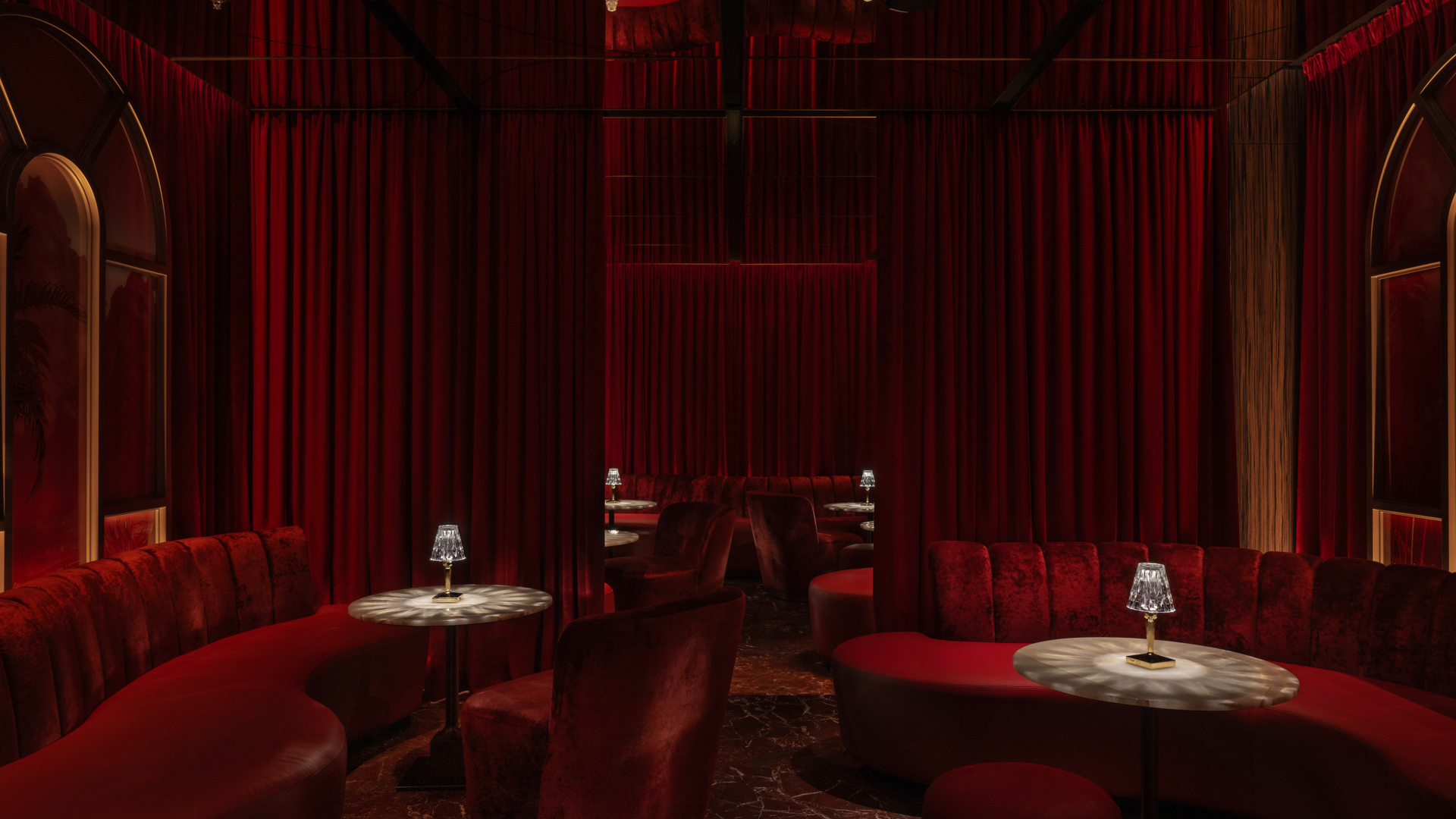 Luxurious red velvet seating surrounds tables with lamps in Banyan Tree Dubai's elegant Rose Bar.