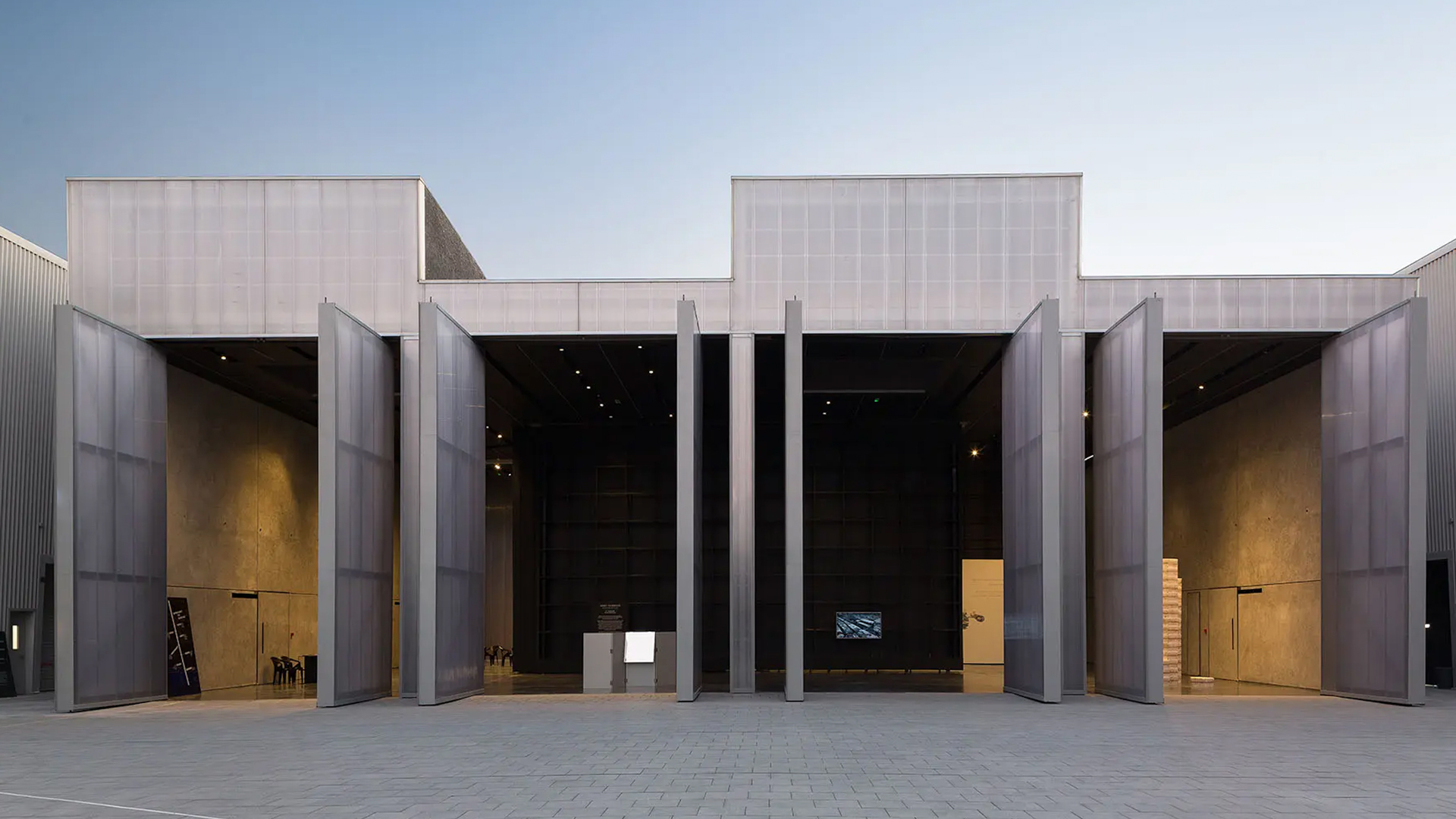 Modern industrial-style building at Alserkal Avenue in Dubai, featuring large open metal-framed doors and minimalist concrete walls. The contemporary architecture, with its clean lines and open gallery-style space, reflects a creative cultural hub for art, design, and innovation.