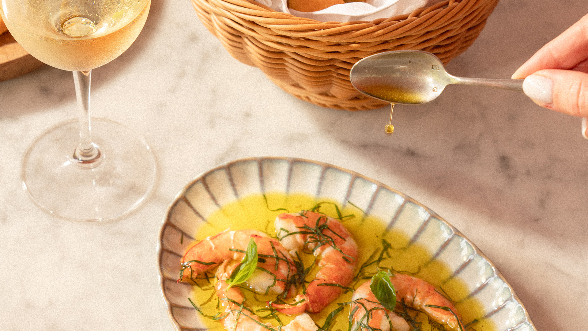 Close-up of a gourmet prawn dish drizzled with olive oil, served with fresh herbs and accompanied by white wine and artisanal bread at Alizée, Banyan Tree Dubai.