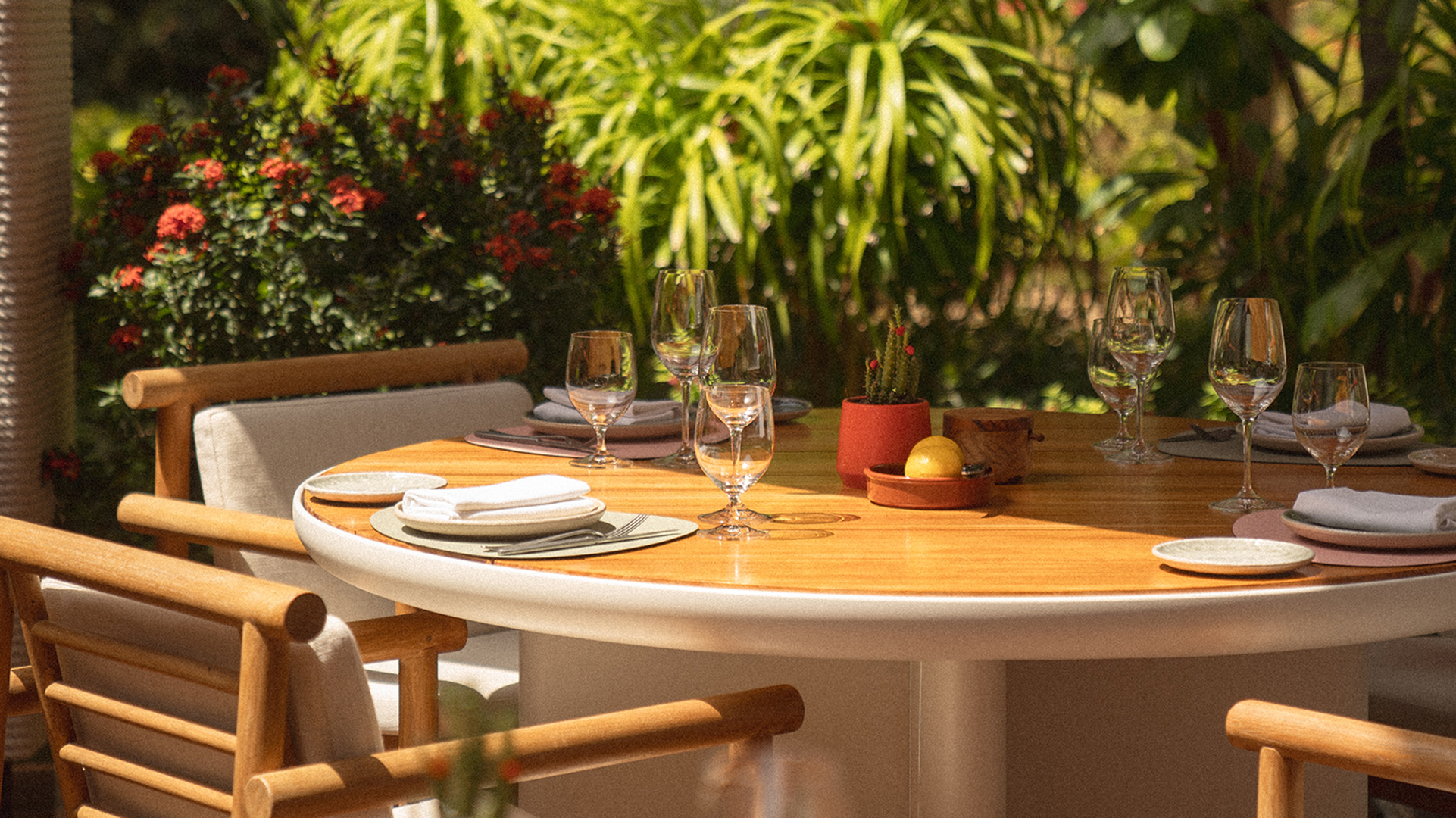 Elegant outdoor dining setup at Alizée, Banyan Tree Dubai, featuring a round wooden table with contemporary chairs, fine glassware, and lush garden surroundings.