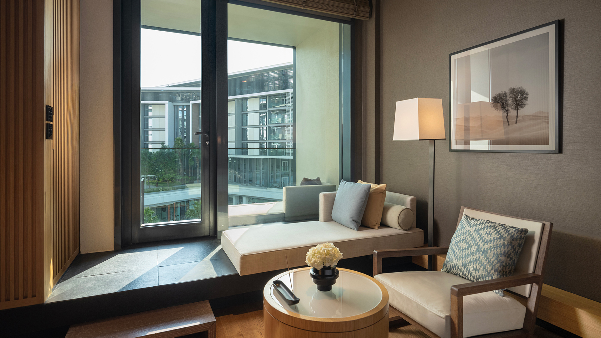 Cozy indoor seating area in Banyan Tree Dubai’s Bliss Guestroom with modern Arabian décor, floor-to-ceiling windows, and private balcony overlooking the resort courtyard.