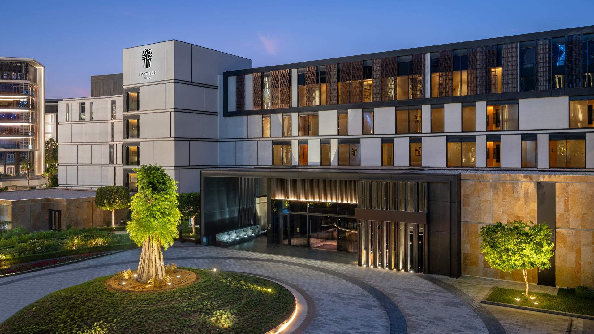 Evening view of Banyan Tree Dubai’s main entrance showcasing modern architecture, ambient lighting, and the iconic banyan tree sculpture in the landscaped arrival area.