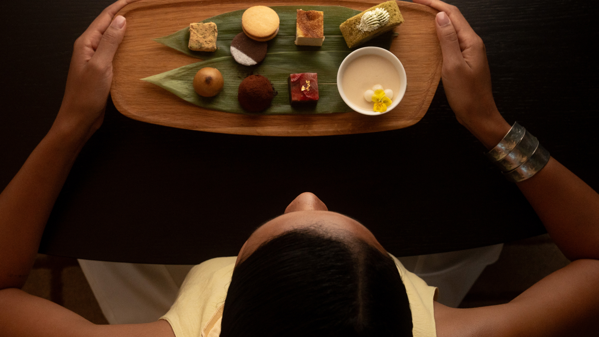 bt-dubai-gallery-dining Guest enjoying an elegant Asian-inspired afternoon tea selection at Tocha, featuring artisanal sweets and a delicate dessert sauce on a wooden tray.