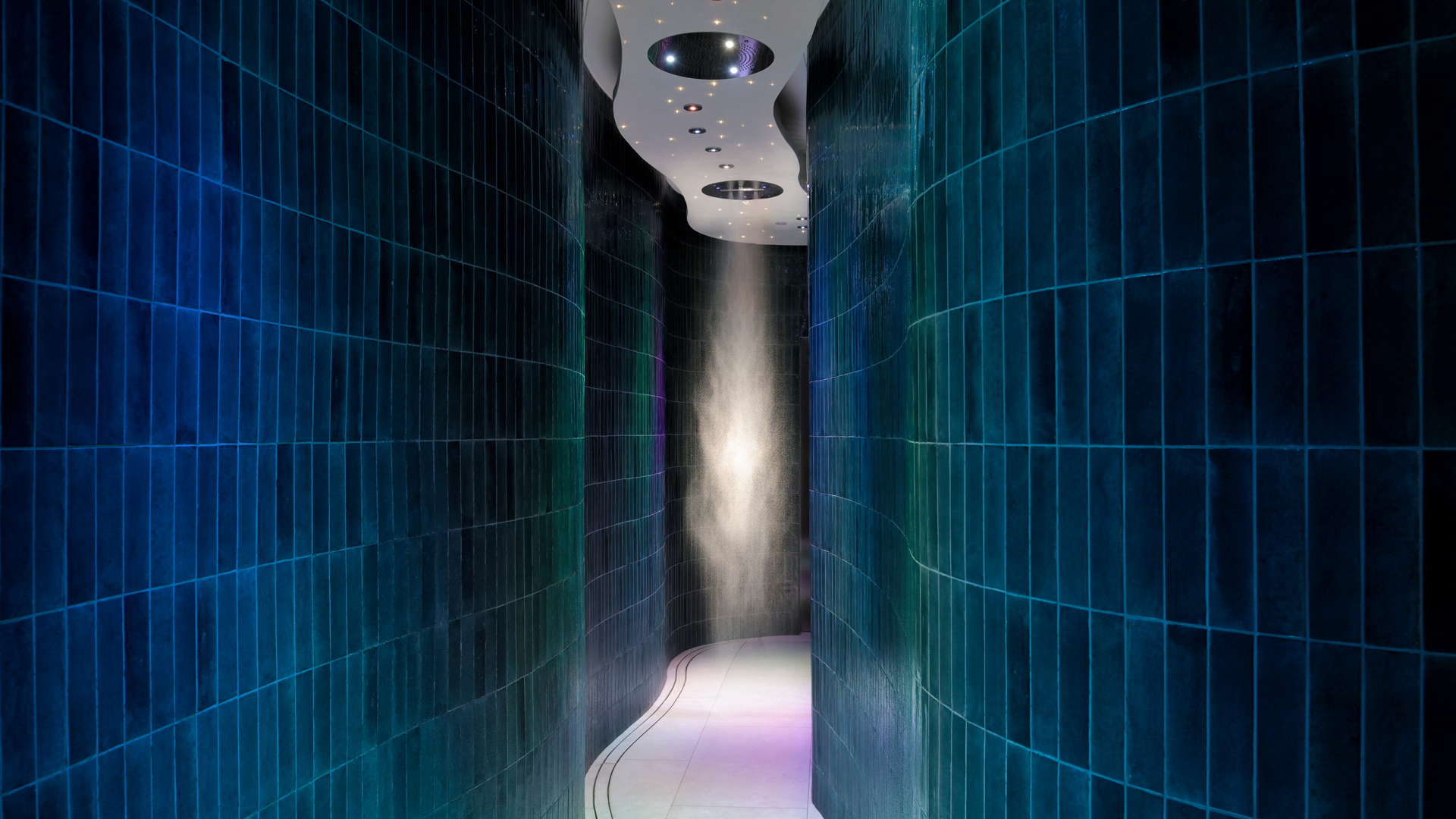 Rain walk-through experience with ambient lighting at Banyan Tree Dubai spa, featuring curved green-tiled walls and ceiling-mounted tropical rain mist showers for immersive hydrotherapy.