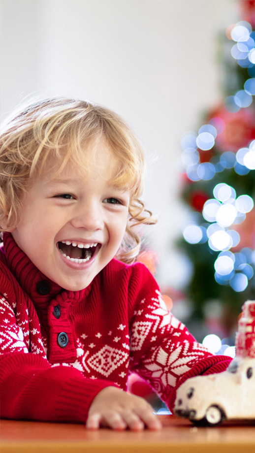 A little boy in a festive jumper playing happily by a christmas tree