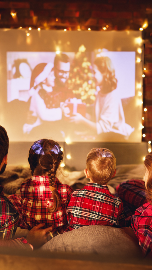 A family watch a movie surrounded by fairy lights