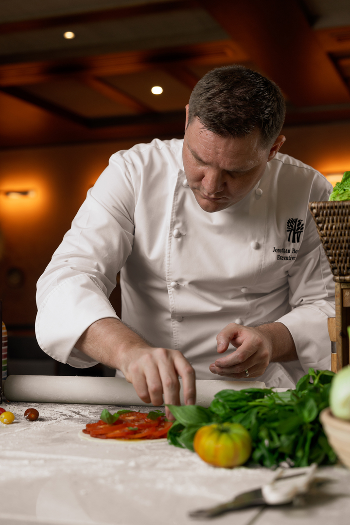 bt-dubai-resort-experiences-jonathan Executive Chef Jonathan Boushall of Banyan Tree Dubai carefully garnishing a tomato-based dish in a warm, ambient kitchen setting, surrounded by fresh herbs and vegetables.