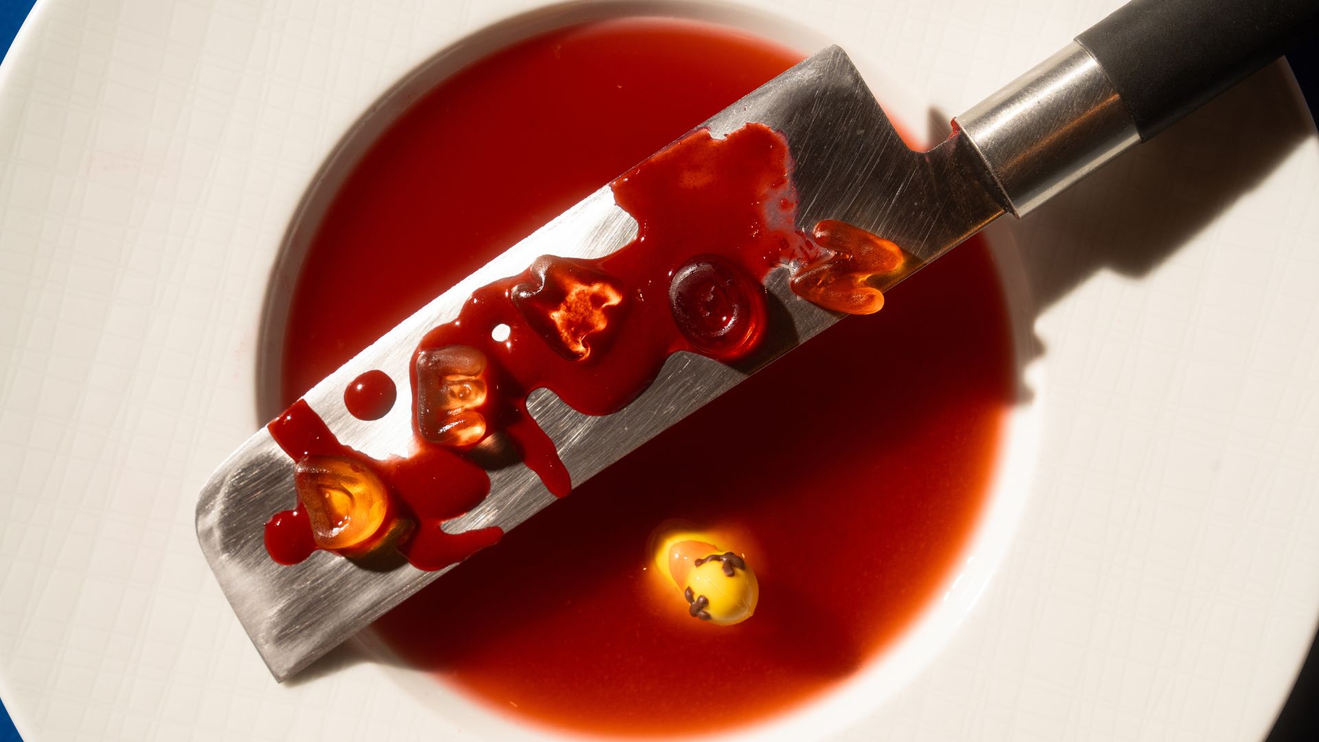 Artistic culinary presentation at Demon Duck, Banyan Tree Dubai — a chef’s knife with vibrant red sauce and garnishes served on a white plate.