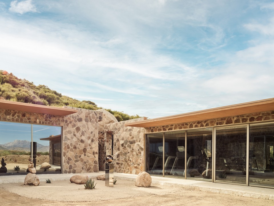 Stone-clad wellness building at Veya de Guadalupe with large glass windows overlooking the desert landscape