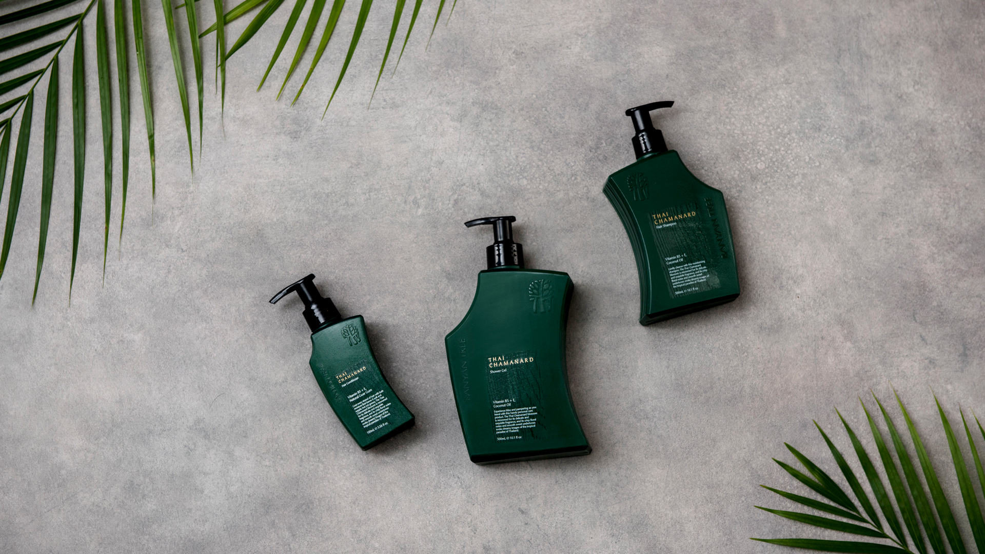 Flat lay of Banyan Tree Thai Chamanard spa product bottles arranged on a textured surface with tropical palm leaves.