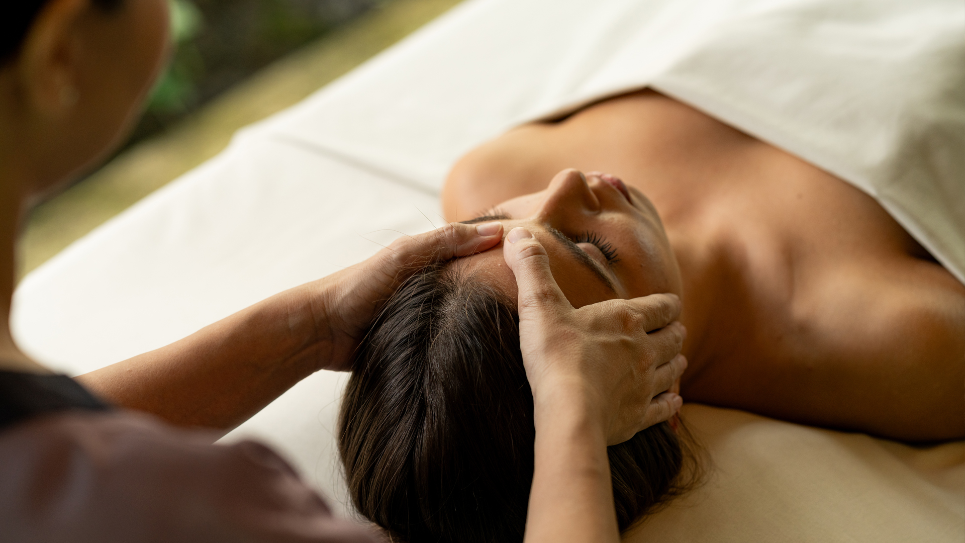 Guest receiving a relaxing head massage at a spa, with a therapist gently applying pressure to the temples.