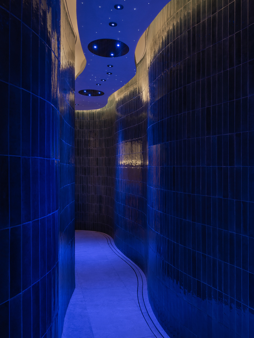 Curved hallway in a luxury spa illuminated by deep blue lighting, creating a tranquil and immersive ambiance.