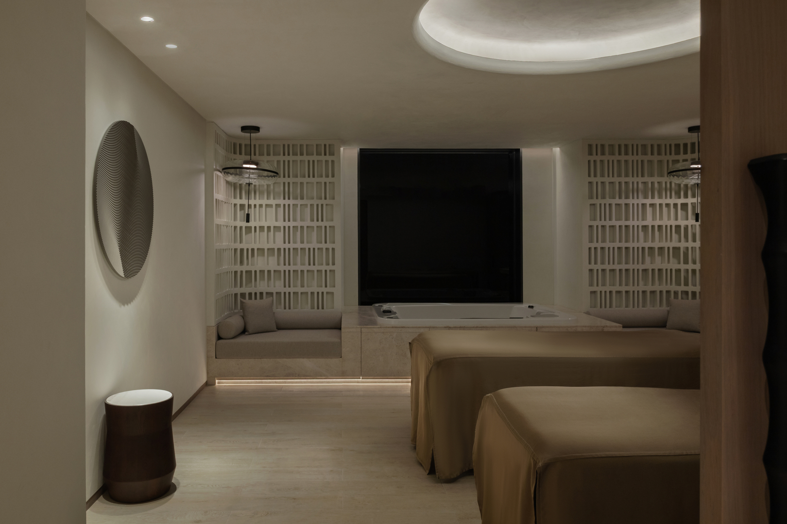 Luxurious spa treatment room featuring two massage beds, soft ambient lighting, built-in seating, and a private whirlpool tub for relaxation.