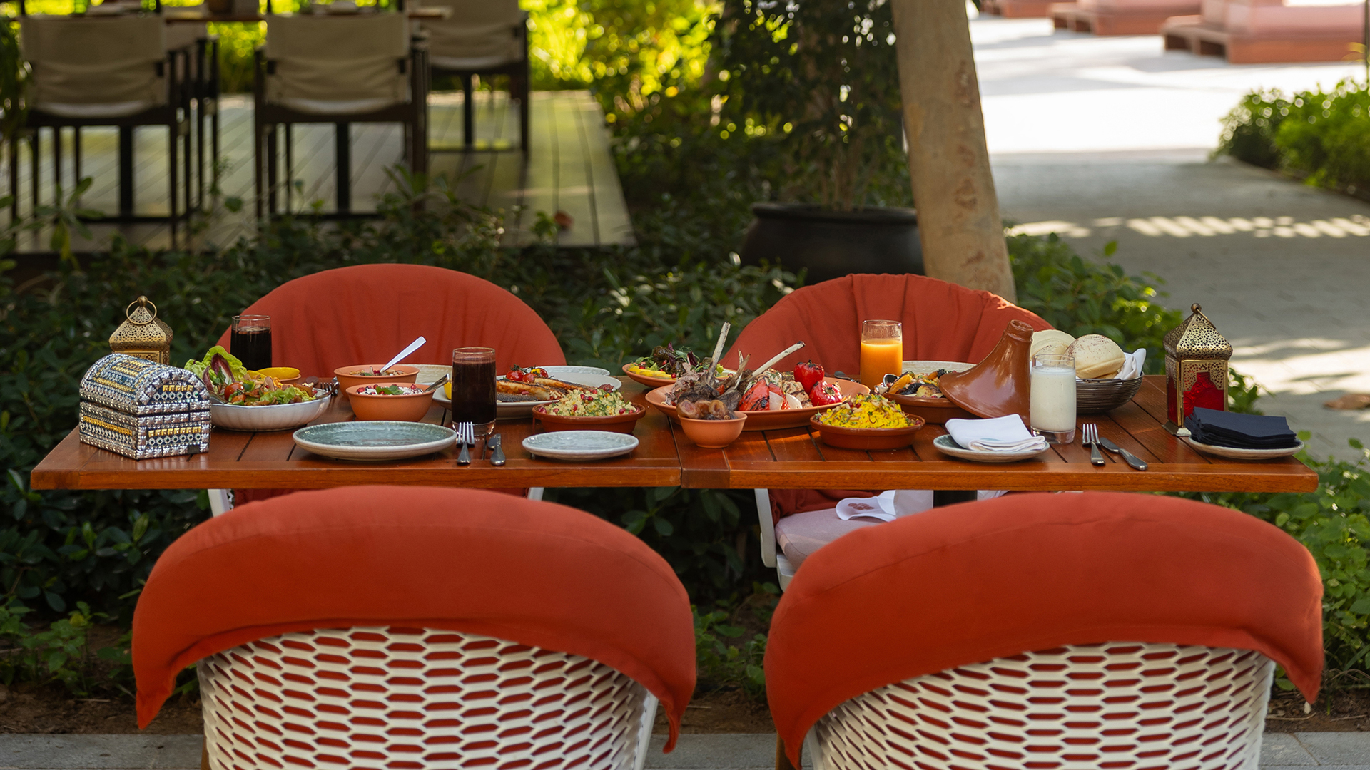 An outdoor dining table set with a variety of Middle Eastern dishes, colourful cushions and drinks, creating a relaxed garden dining atmosphere.